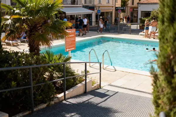 Piscine extérieure entourée de palmiers, avec des personnes se baignant et se détendant sur le bord.