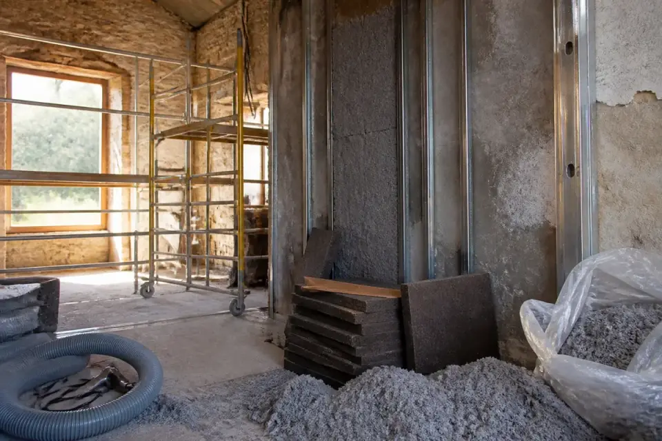 Rénovation intérieure avec échafaudage et matériaux d'isolation, mur en pierre, et fenêtre ensoleillée.