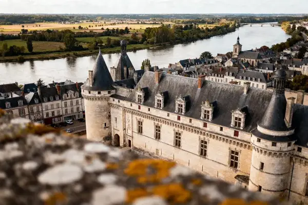 Vue aérienne d'un château historique, rivière et campagne environnante, architecture médiévale, ciel dégagé.