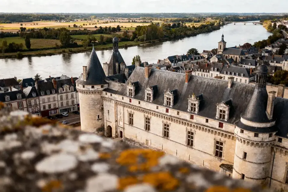 Vue aérienne d'un château historique, rivière et campagne environnante, architecture médiévale, ciel dégagé.