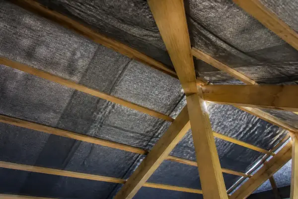 Structure de toiture avec poutres en bois et bâche noire tendue pour une isolation optimale.