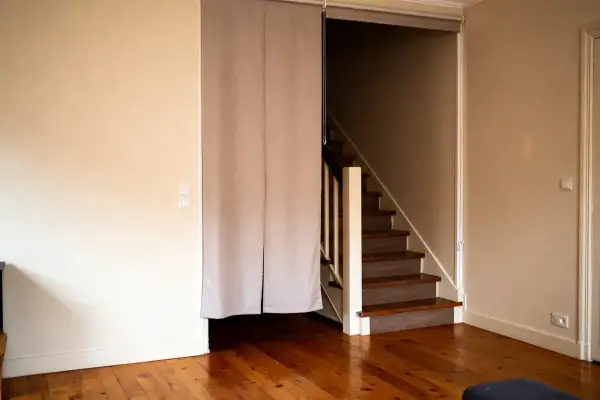 Escalier en bois avec rideau beige, plancher en bois, murs clairs, intérieur de maison.