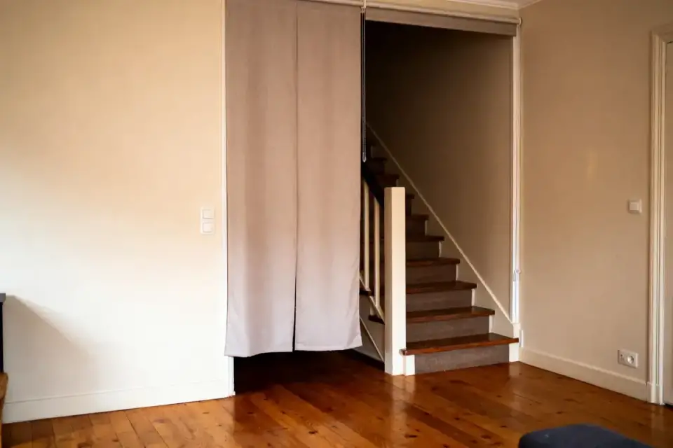 Escalier en bois avec rideau beige, plancher en bois, murs clairs, intérieur de maison.