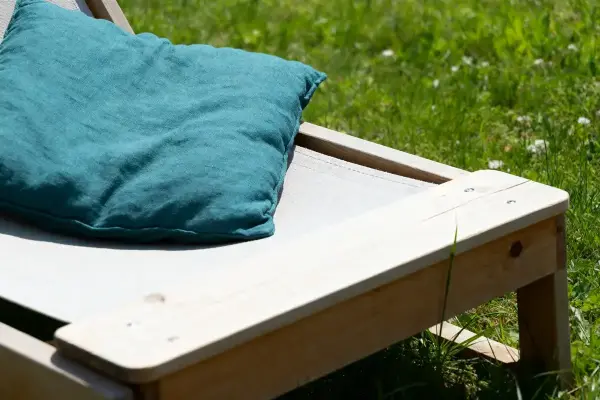 Chaise longue en bois avec coussin turquoise sur pelouse verte ensoleillée.